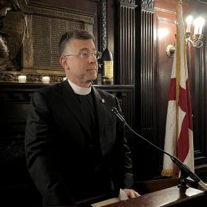 Father Pyles delivers remarks at the Trafalgar Night Dinner from a podium in the Maryland Club's cafe